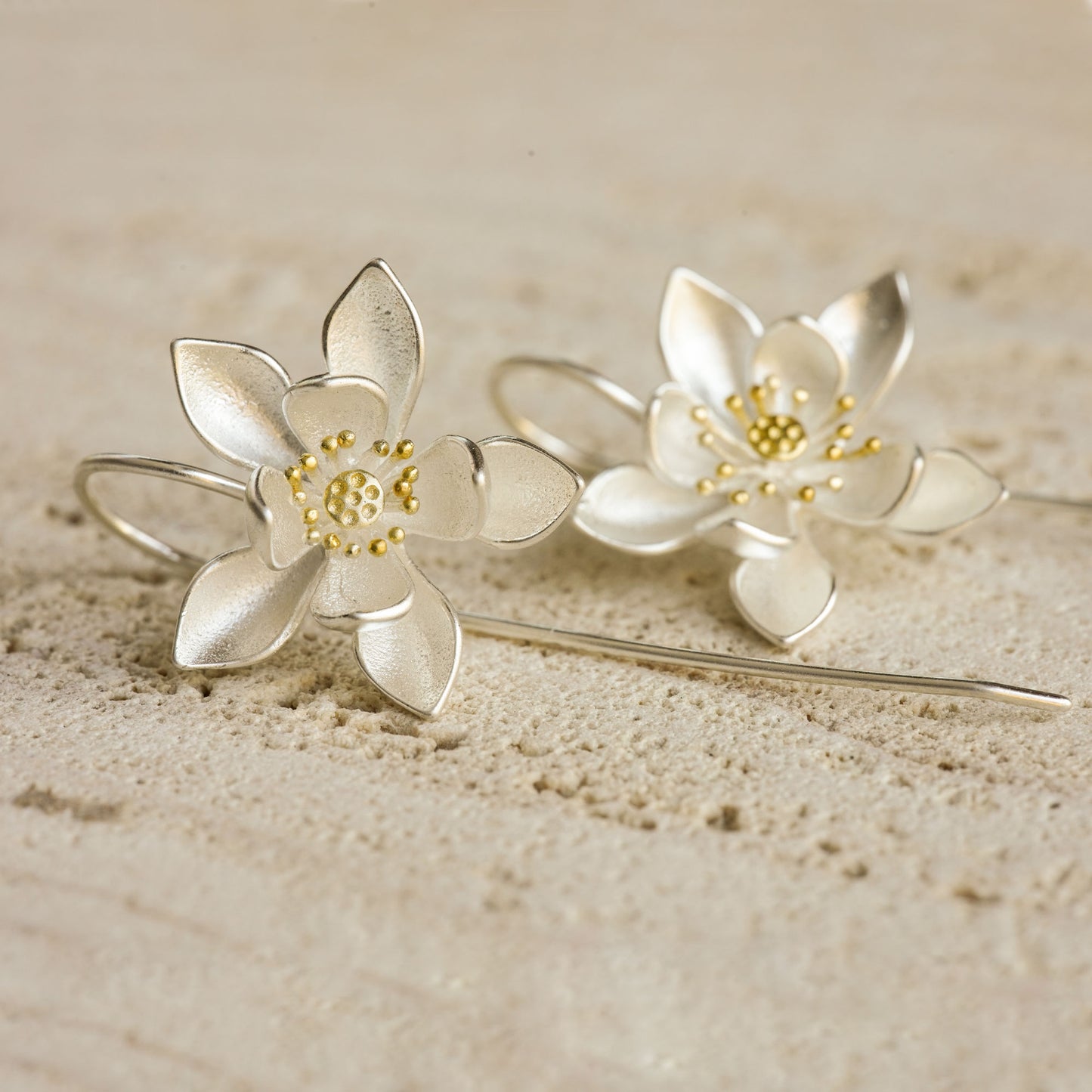 A pair of silver water lily earrings on a stone slab