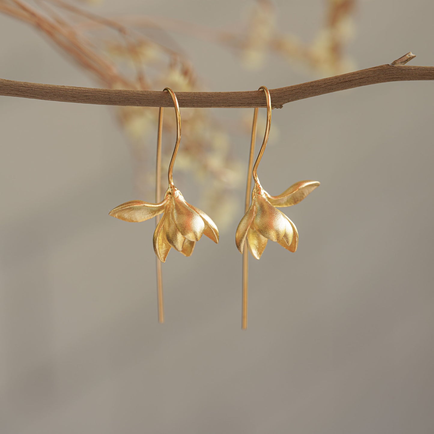 Golden magnolia earrings hanging from a tree branch