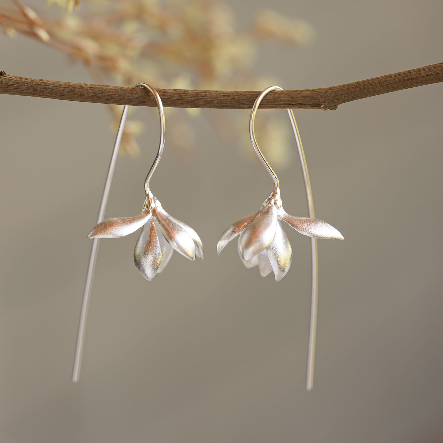 Silver magnolia earrings hanging from a tree branch