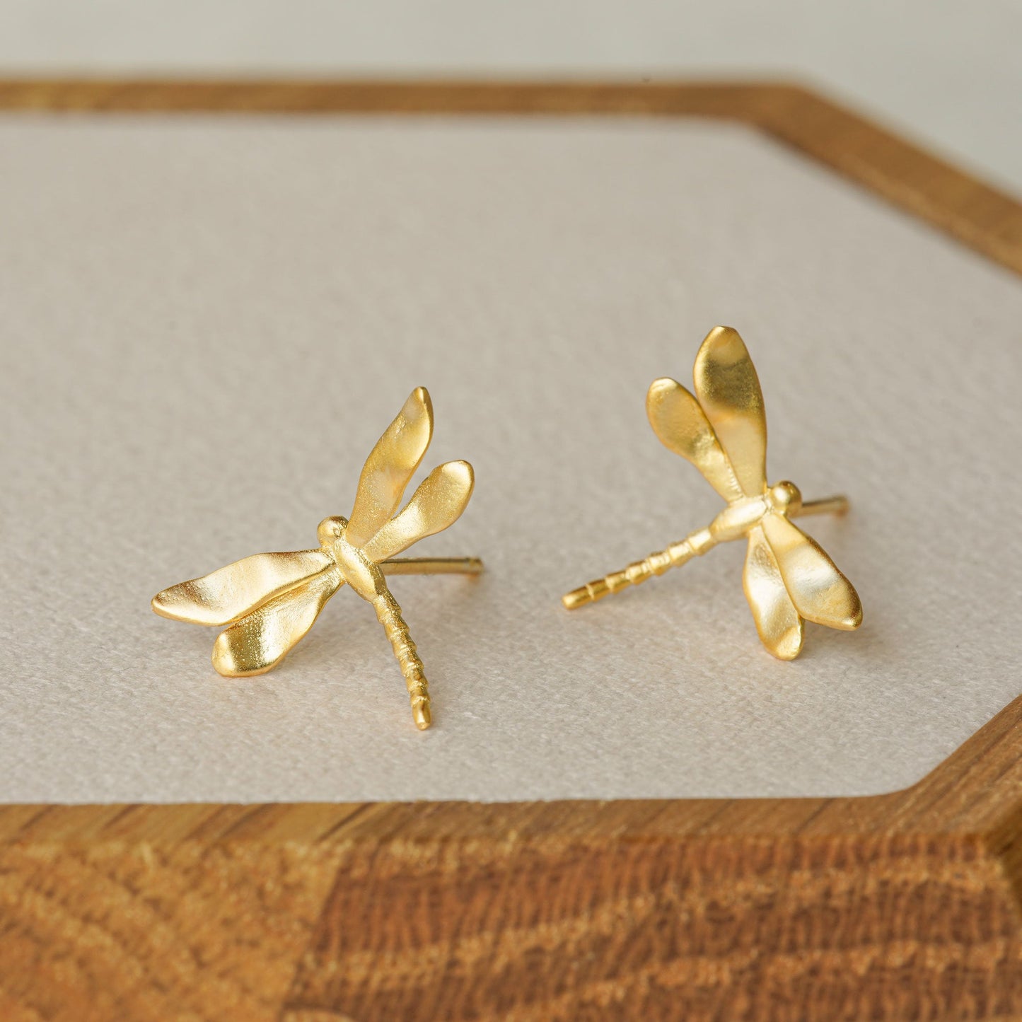 Gold dragonfly stud earrings displayed on a wooden tray, showing their shiny finish and organic wing shape