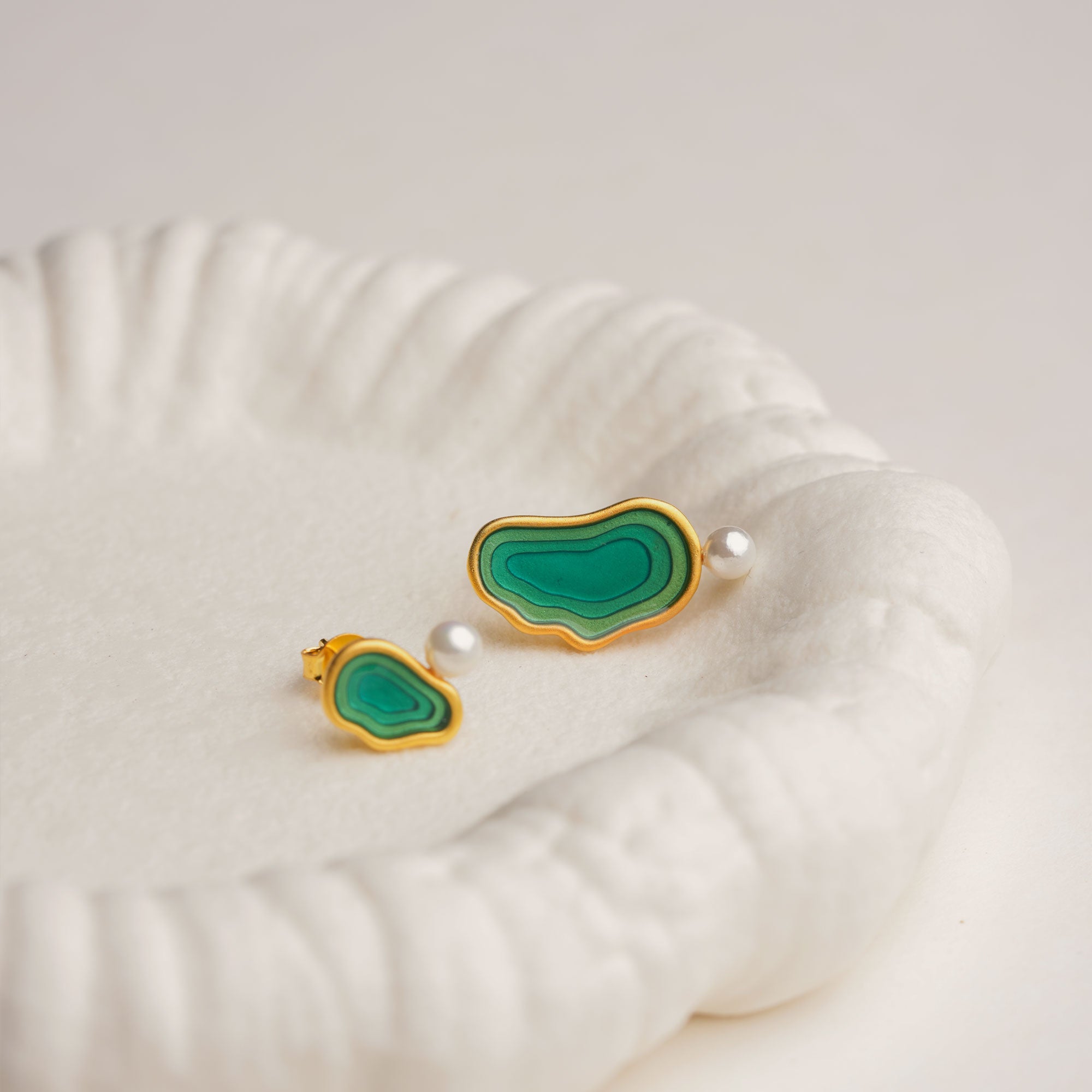 Asymmetrical green resin pearl drop earrings on white dish