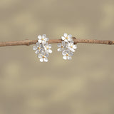 Close-up of 925 silver forget-me-not stud earrings with gold centers on neutral background