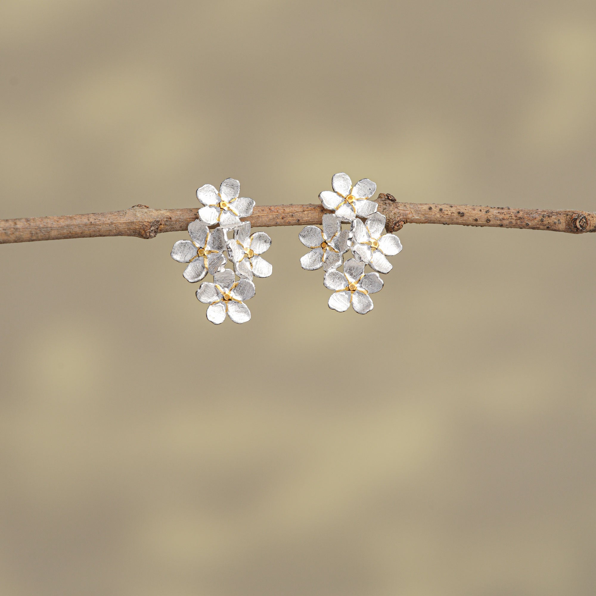 Close-up of 925 silver forget-me-not stud earrings with gold centers on neutral background