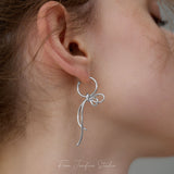 Silver bow dangle earrings displayed as a pair