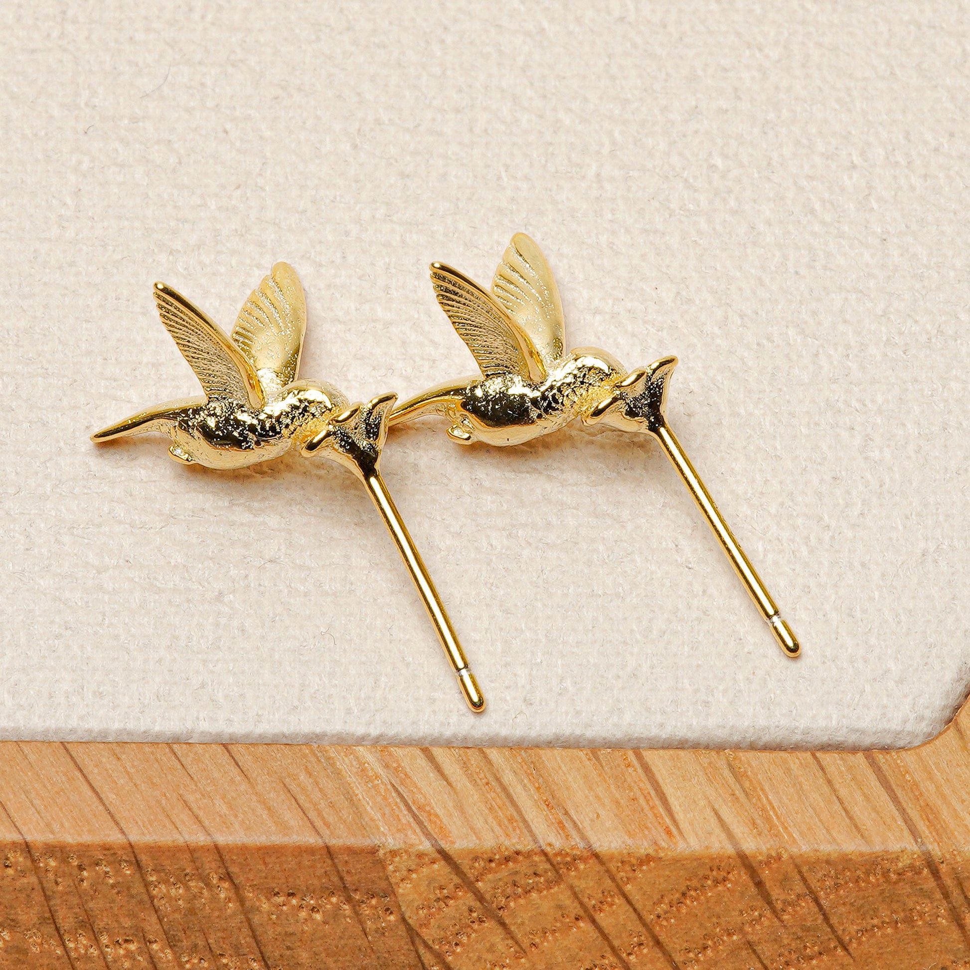 A pair of gold hummingbird earrings on a gray tabletop