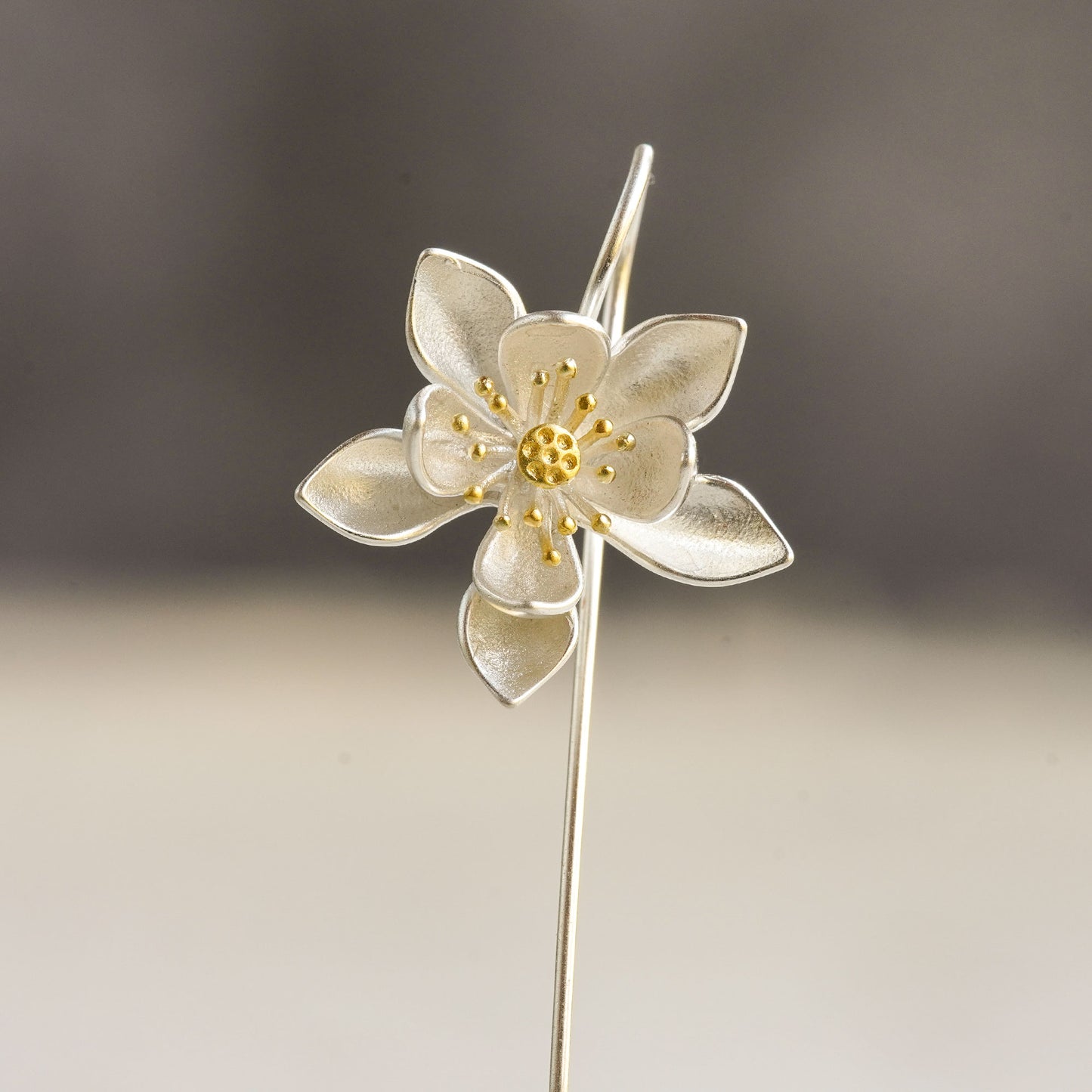 A silver lotus flower earring in front of a gray background