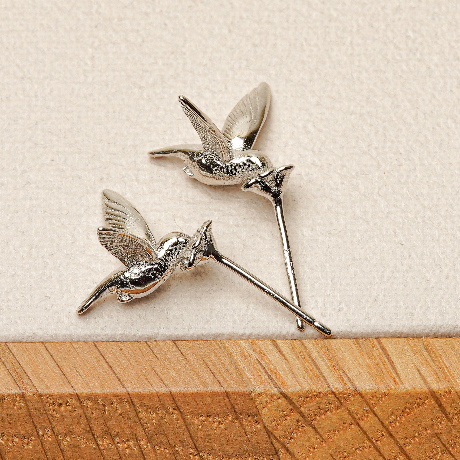 A pair of silver hummingbird earrings on a grey desktop