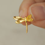 Close-up of a hand holding a gold dragonfly earring with delicate wings and handmade finish
