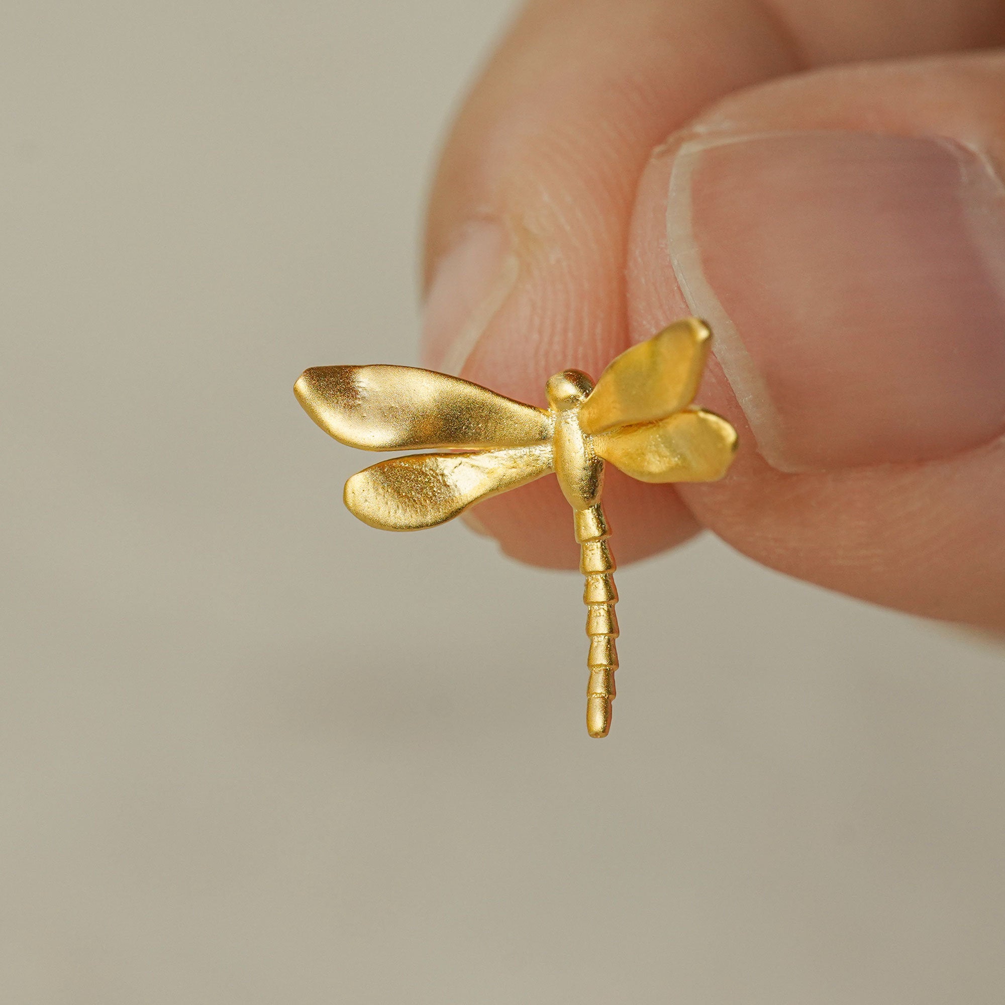 Close-up of a hand holding a gold dragonfly earring with delicate wings and handmade finish