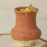 Gold dragonfly stud earrings resting on the rim of a rustic clay vase