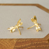 Gold dragonfly stud earrings displayed on a wooden tray