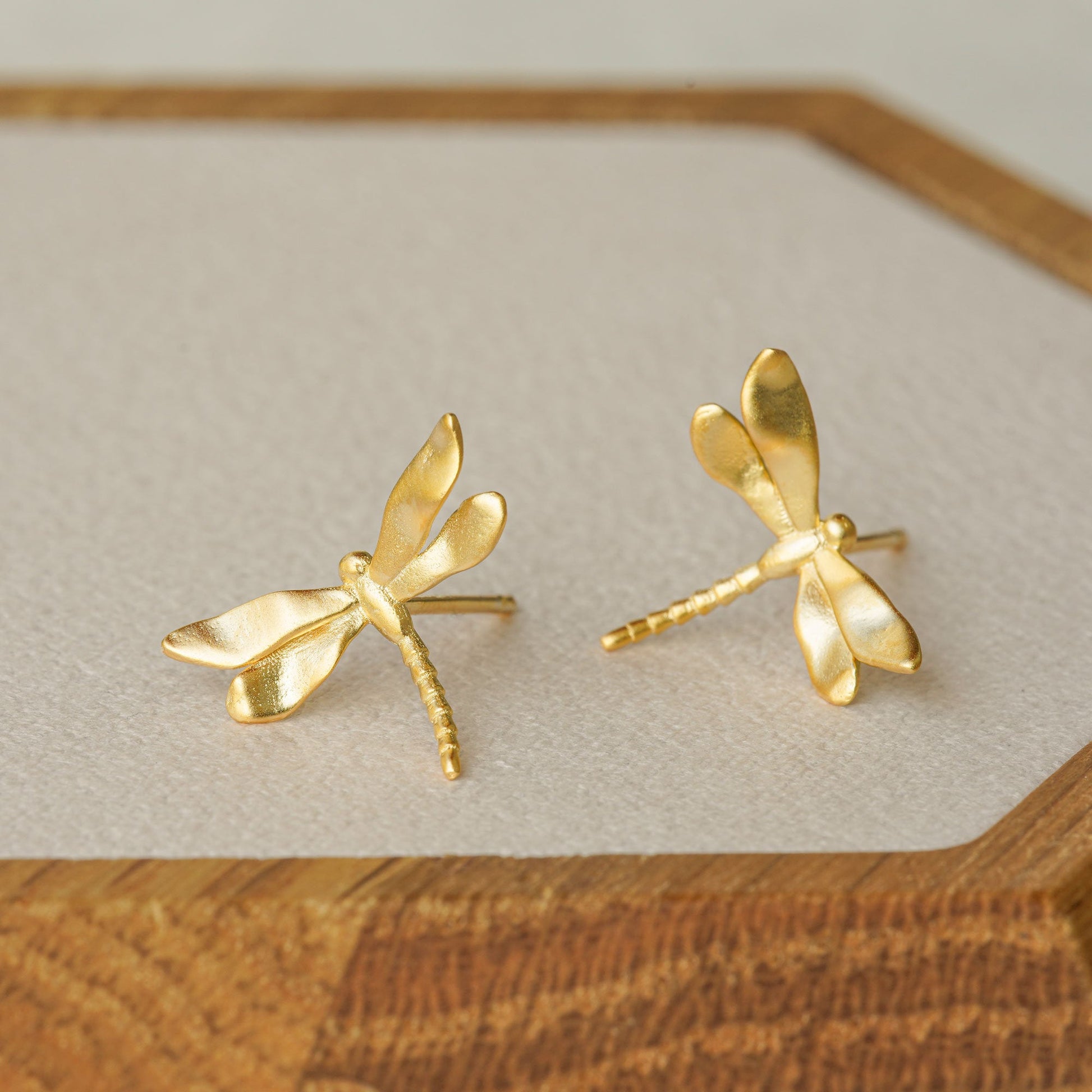 Gold dragonfly stud earrings displayed on a wooden tray, showing their shiny finish and organic wing shape
