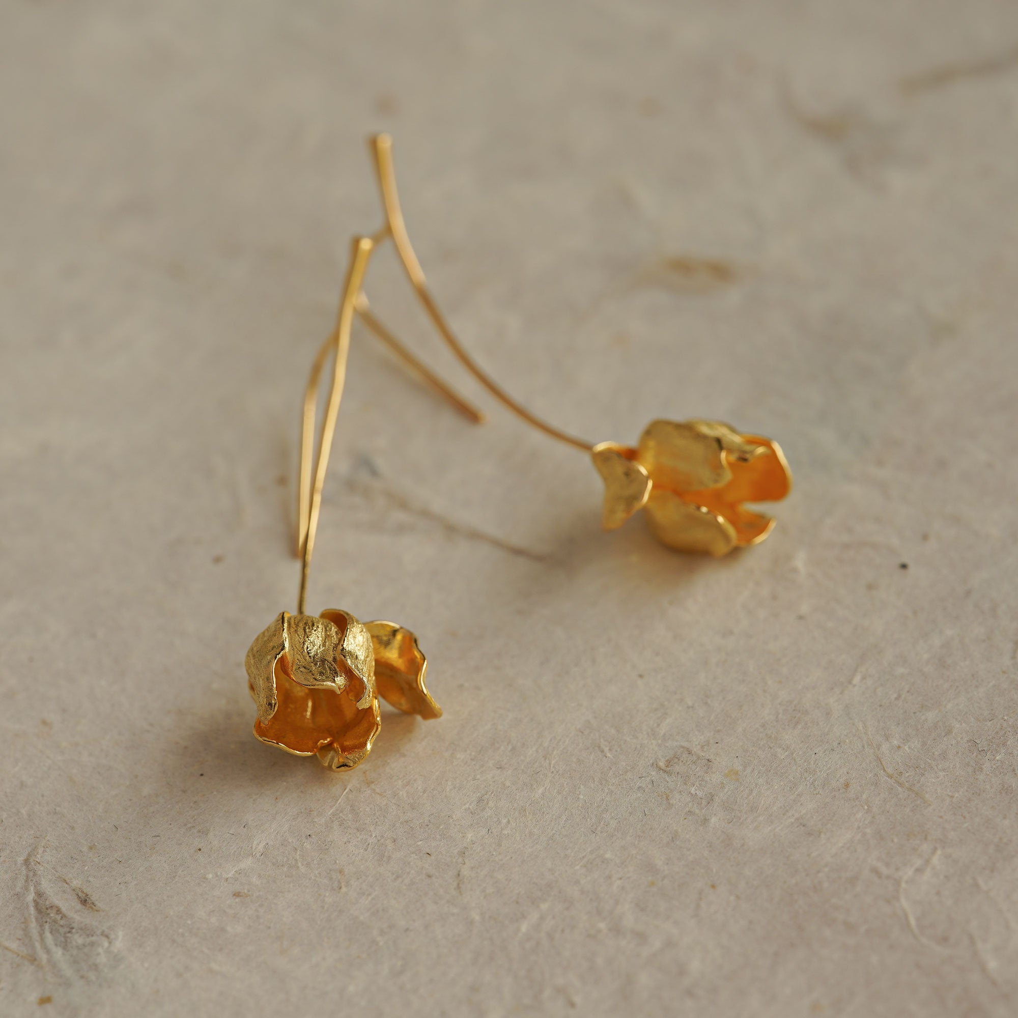 Close-up of gold tulip flower earrings lying flat, highlighting organic petal texture and handmade finish