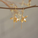 Golden magnolia earrings hanging from a tree branch