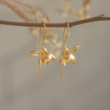 Golden magnolia earrings hanging from a tree branch