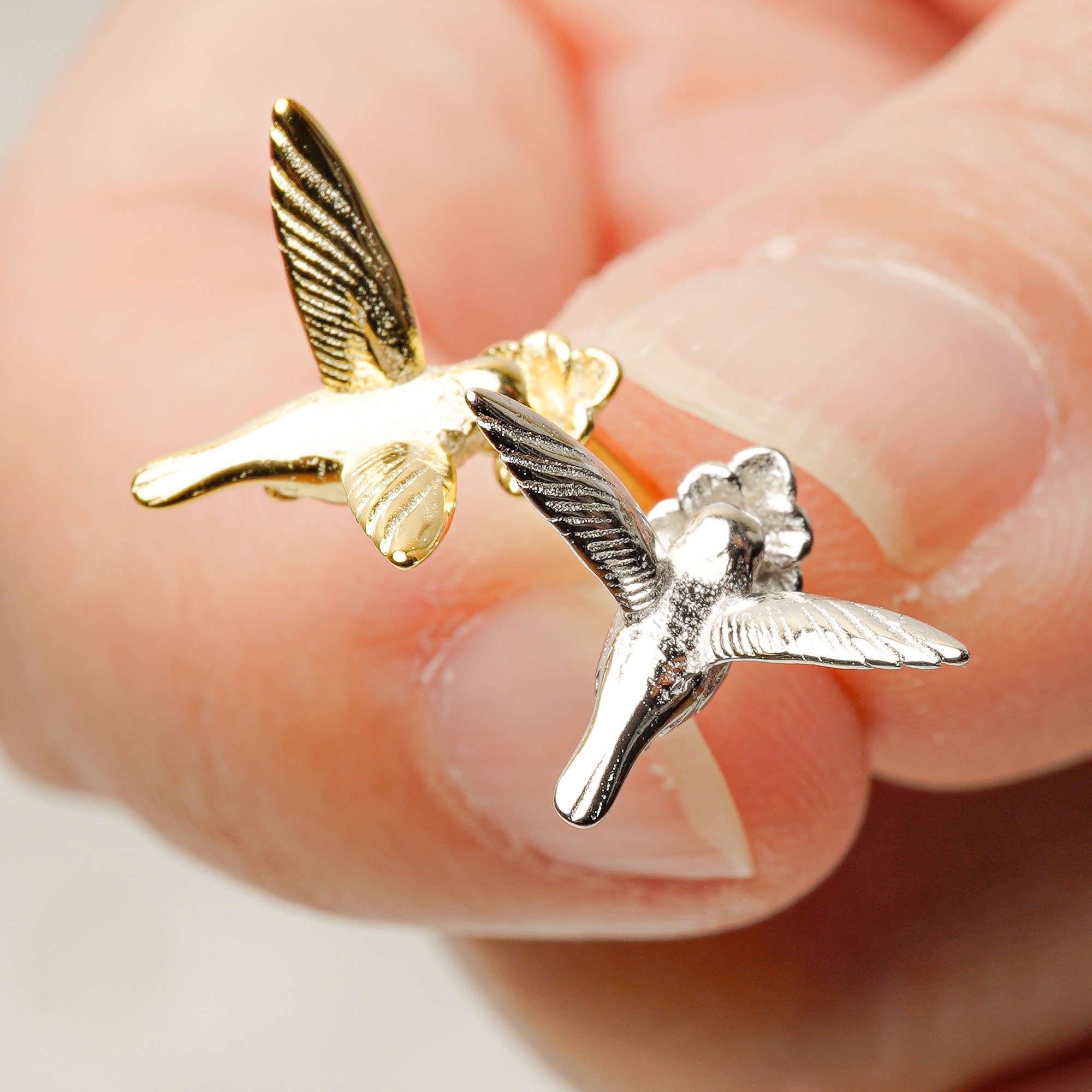 Hand holding a pair of tiny hummingbird earrings