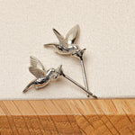 A pair of silver hummingbird earrings on a grey desktop