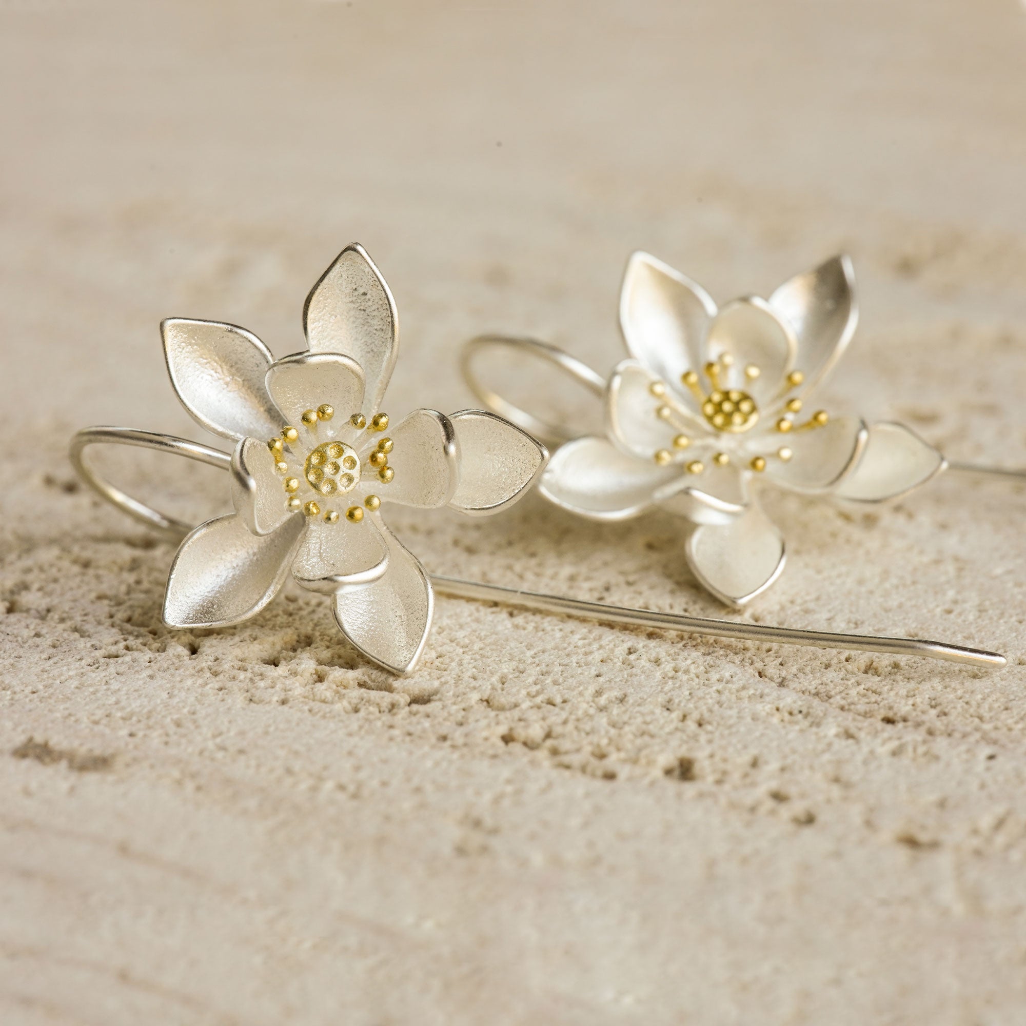 A pair of silver water lily earrings on a stone slab