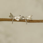 Silver dragonfly stud earrings displayed on a wooden branch