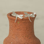 Silver dragonfly stud earrings displayed on the rim of a rustic clay vase