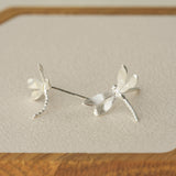 Silver dragonfly stud earrings displayed on a wooden tray, highlighting their delicate shape and textured finish