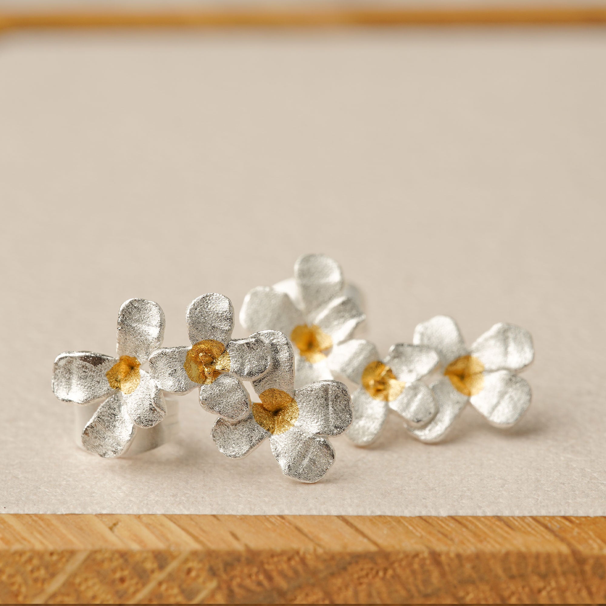 Silver flower earrings on a neutral product background