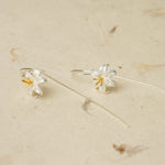 Silver lily drop earrings laid on a neutral textured surface