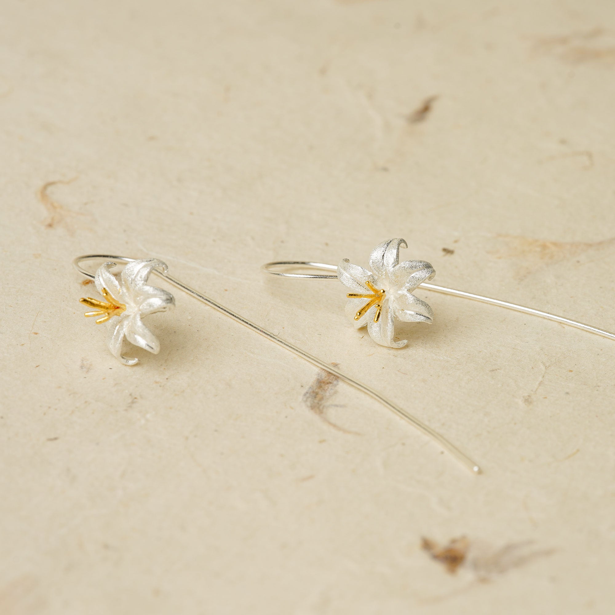 Silver lily drop earrings laid on a neutral textured surface