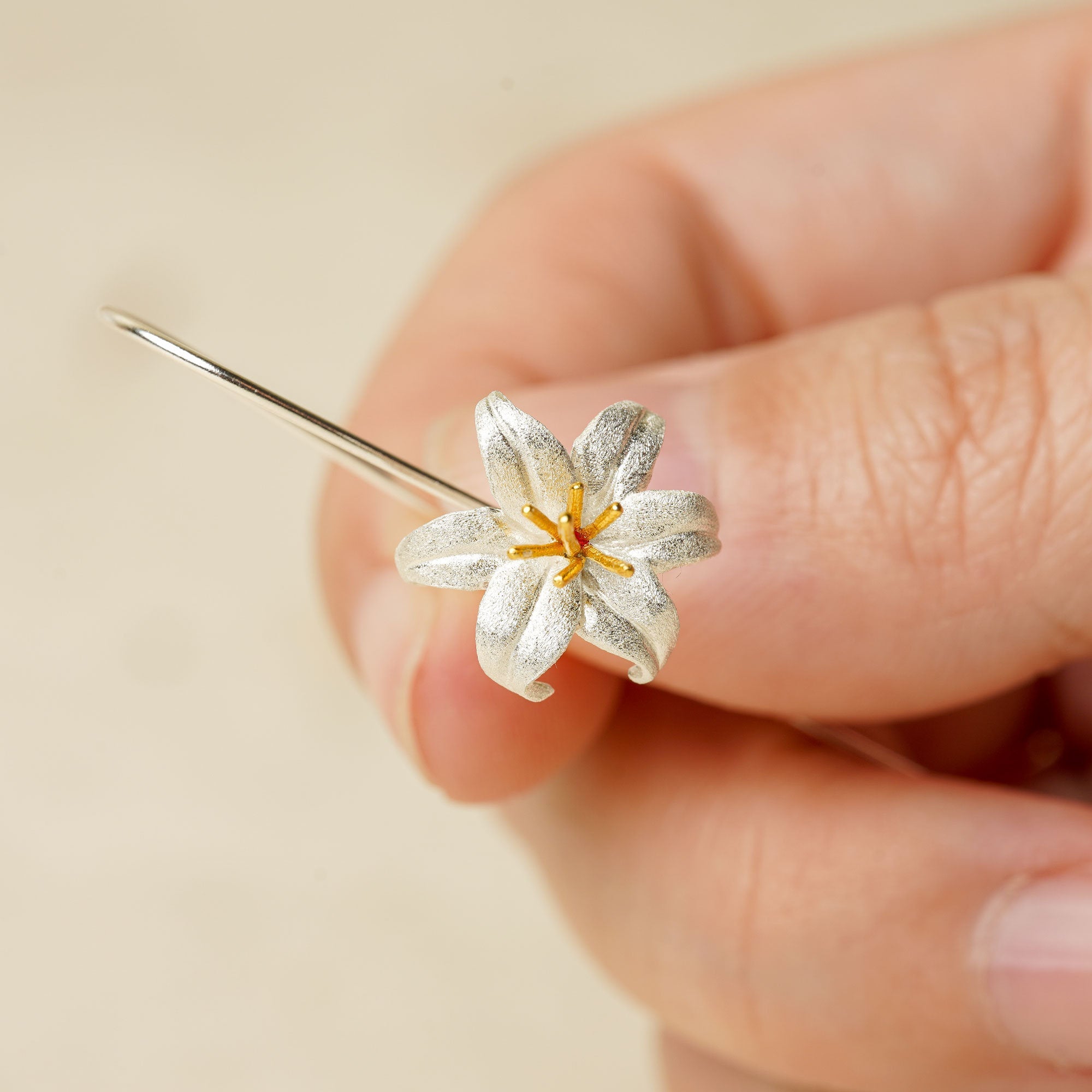 Close-up of a silver lily flower earring showing petal and stamen details