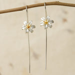 Silver lily flower earrings with gold stamens hanging on a branch