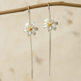 Silver lily flower earrings with gold stamens hanging on a branch