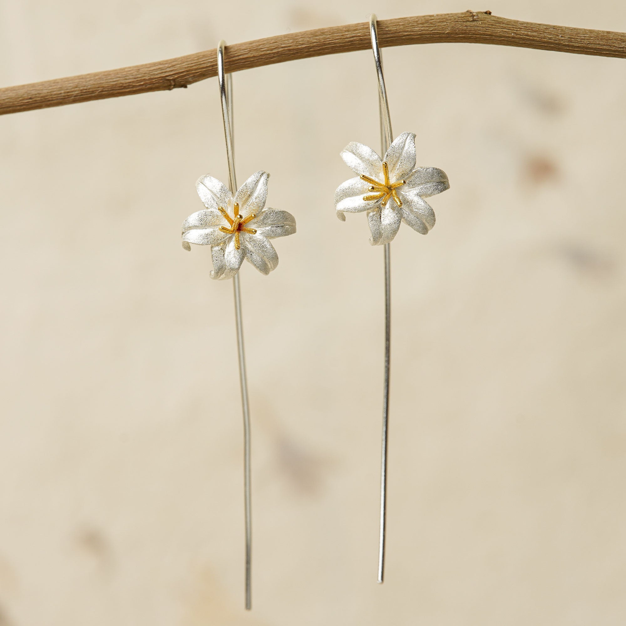 Silver lily flower earrings with gold stamens hanging on a branch