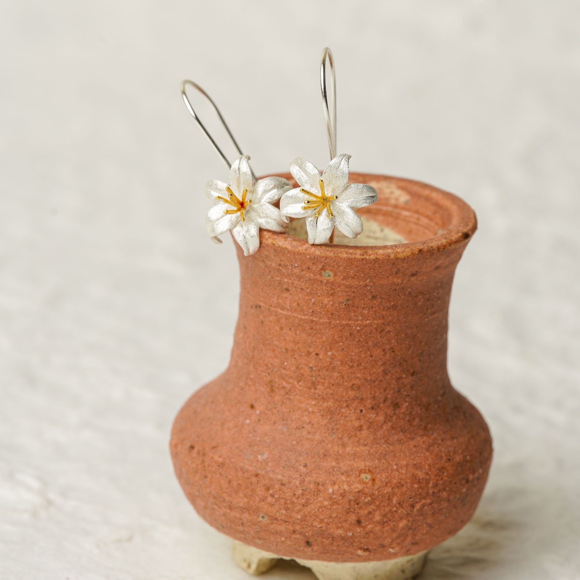 Silver lily flower earrings displayed in a rustic ceramic vase