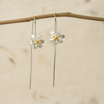 Pair of silver lily flower earrings hanging from a natural branch
