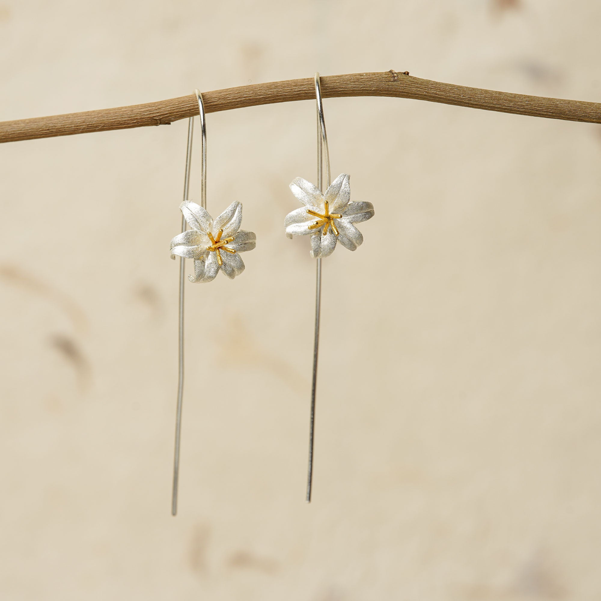 Pair of silver lily flower earrings hanging from a natural branch