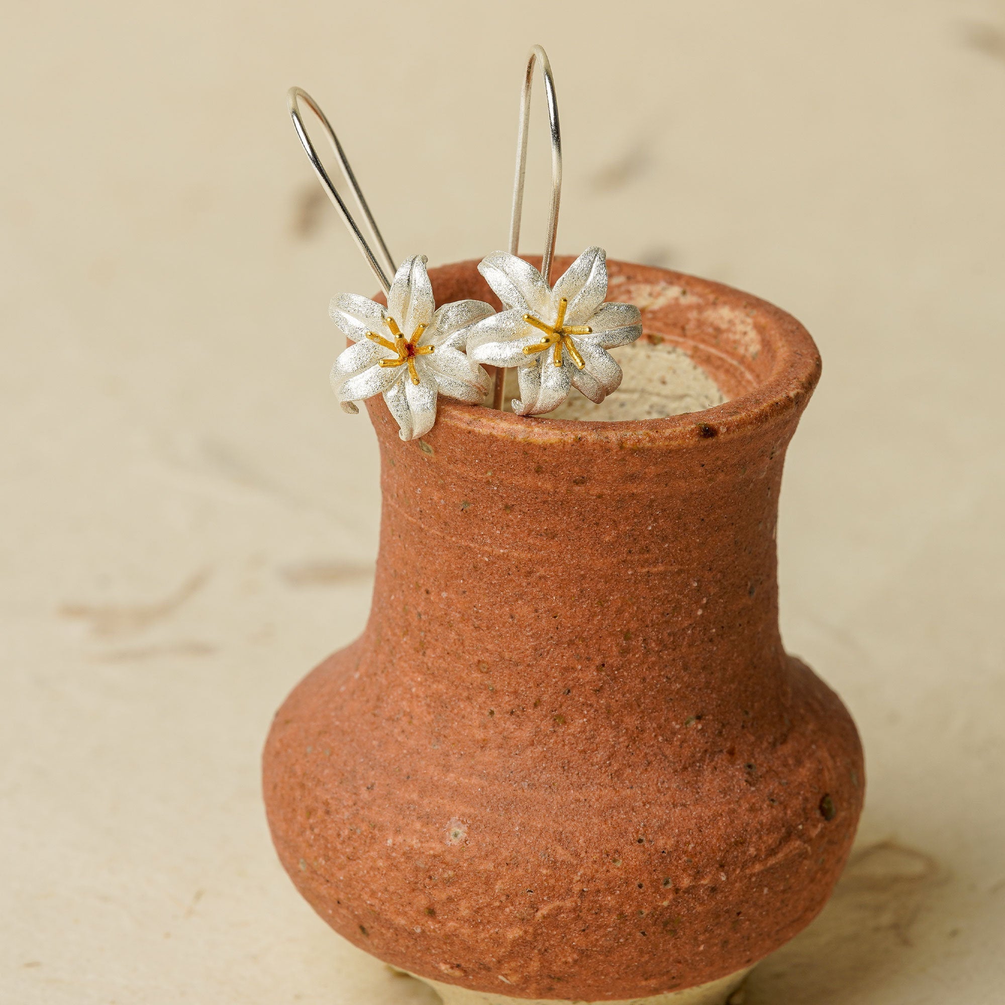 Silver lily flower earrings displayed in a terracotta vase