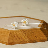 Silver lily flower earrings arranged on a wooden tray