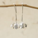 Front view of silver tulip flower earrings hanging on a branch, showcasing delicate petal design