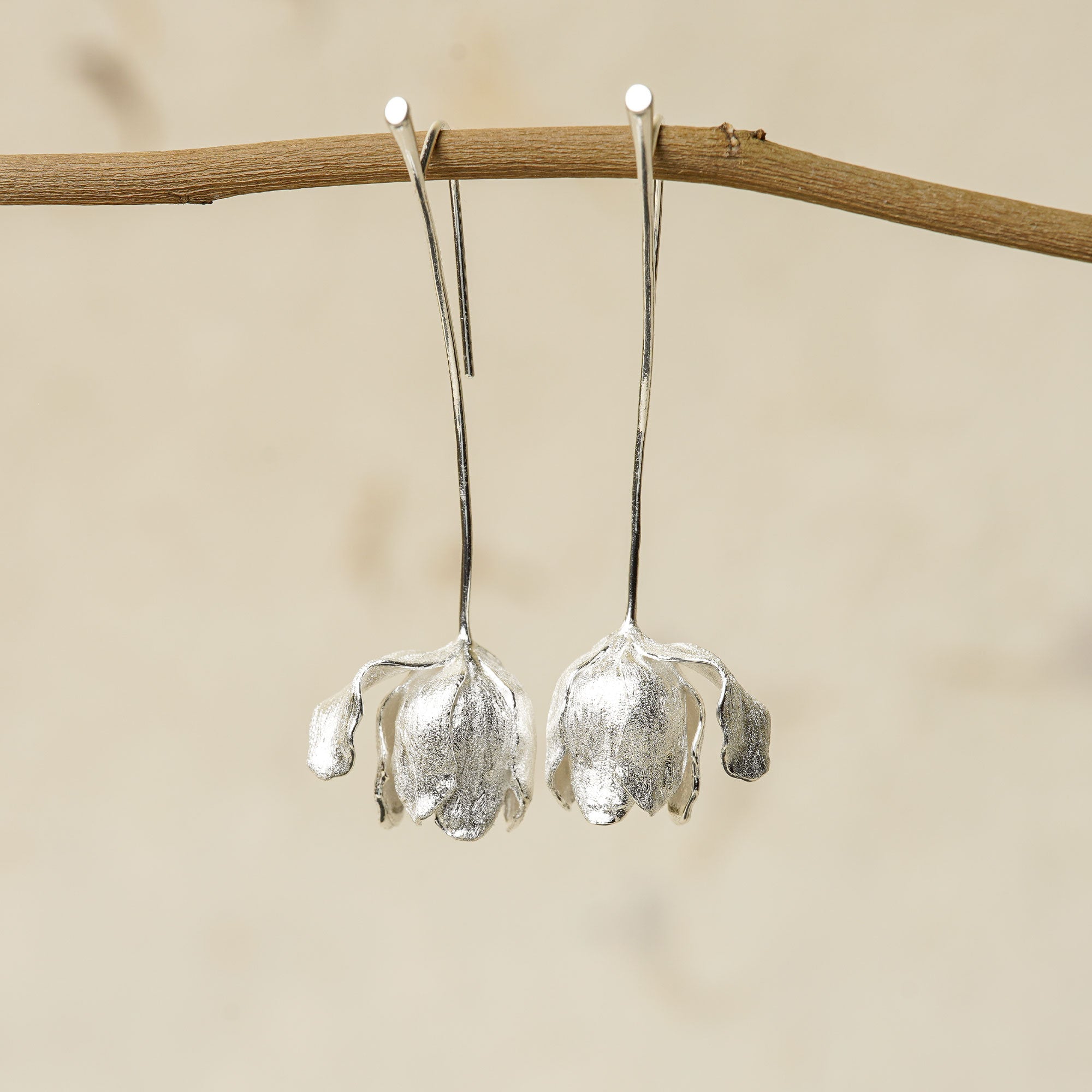 Front view of silver tulip flower earrings hanging on a branch, showcasing delicate petal design