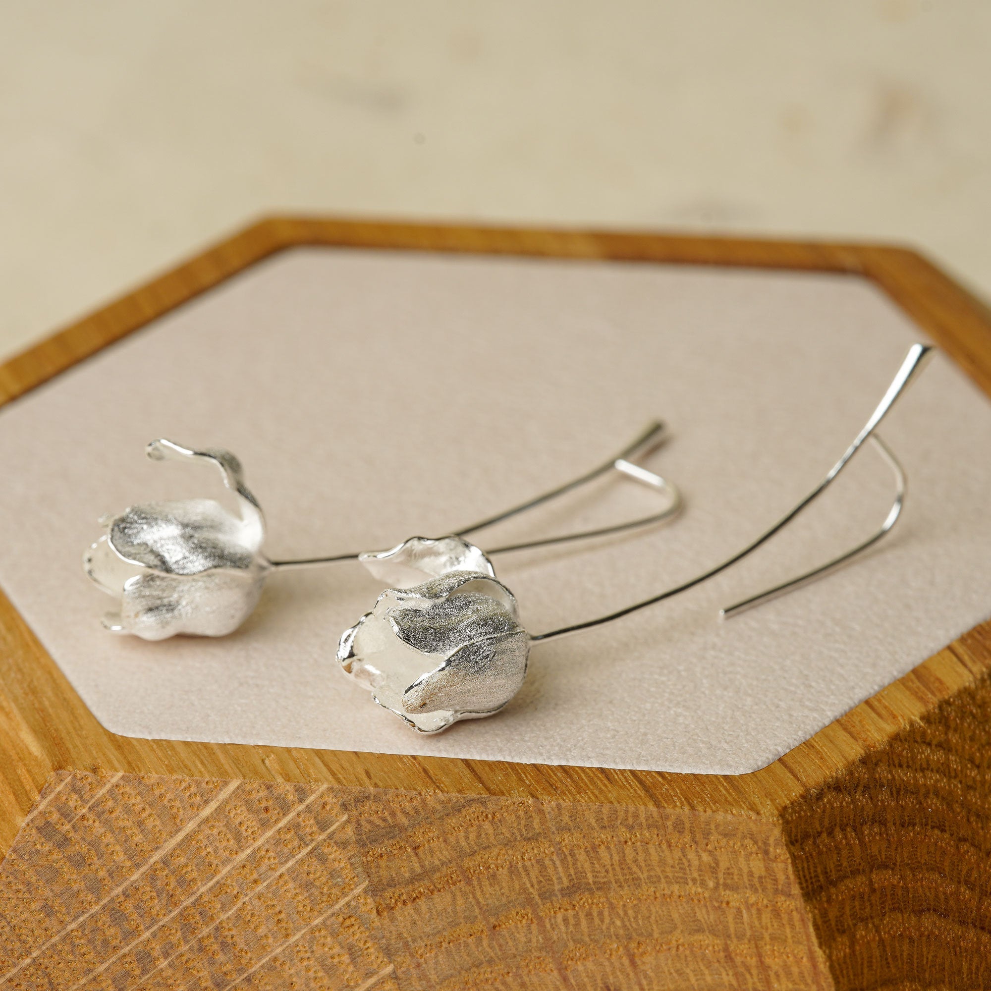 Silver tulip earrings displayed on a wooden tray, highlighting handcrafted flower details