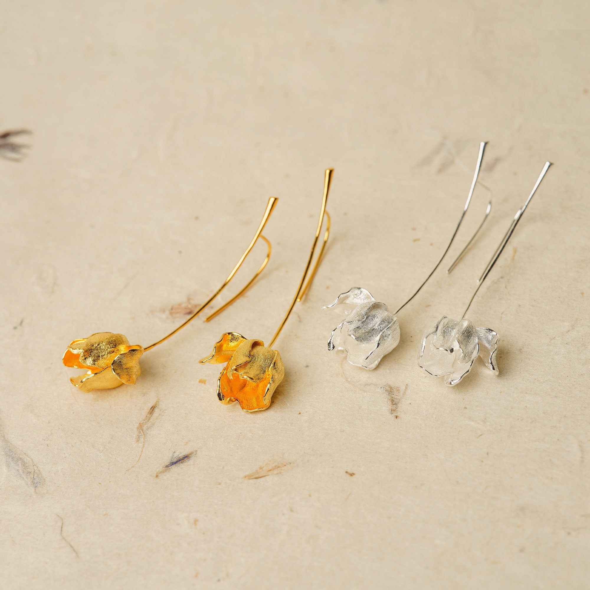 Flatlay of gold and silver tulip flower earrings with long hooks and realistic petal shape