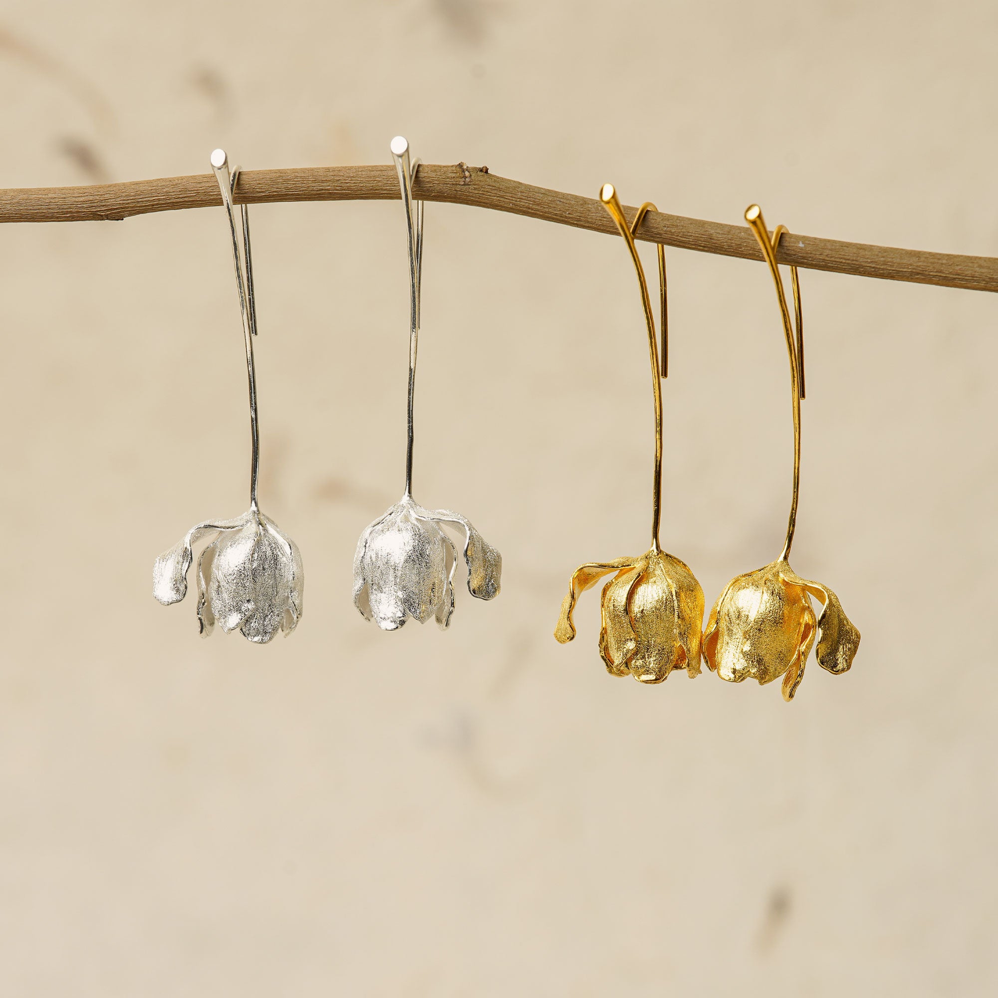 Gold and silver tulip earrings hanging side by side, showing contrast between the two finishes